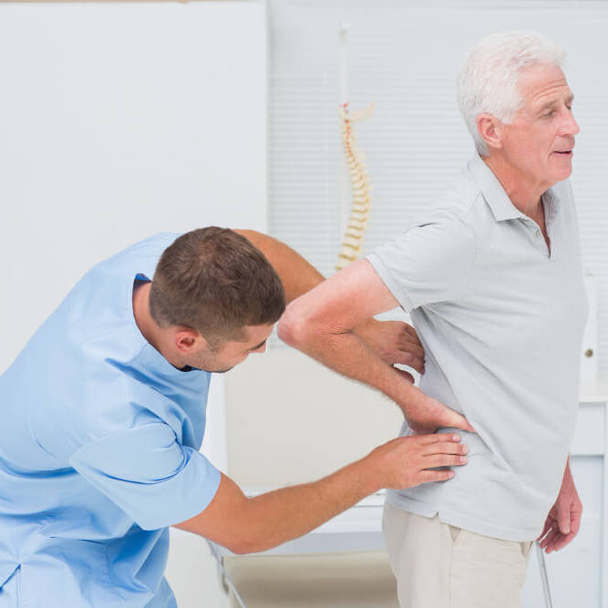 A healthcare professional assisting an elderly man with back pain during a consultation.